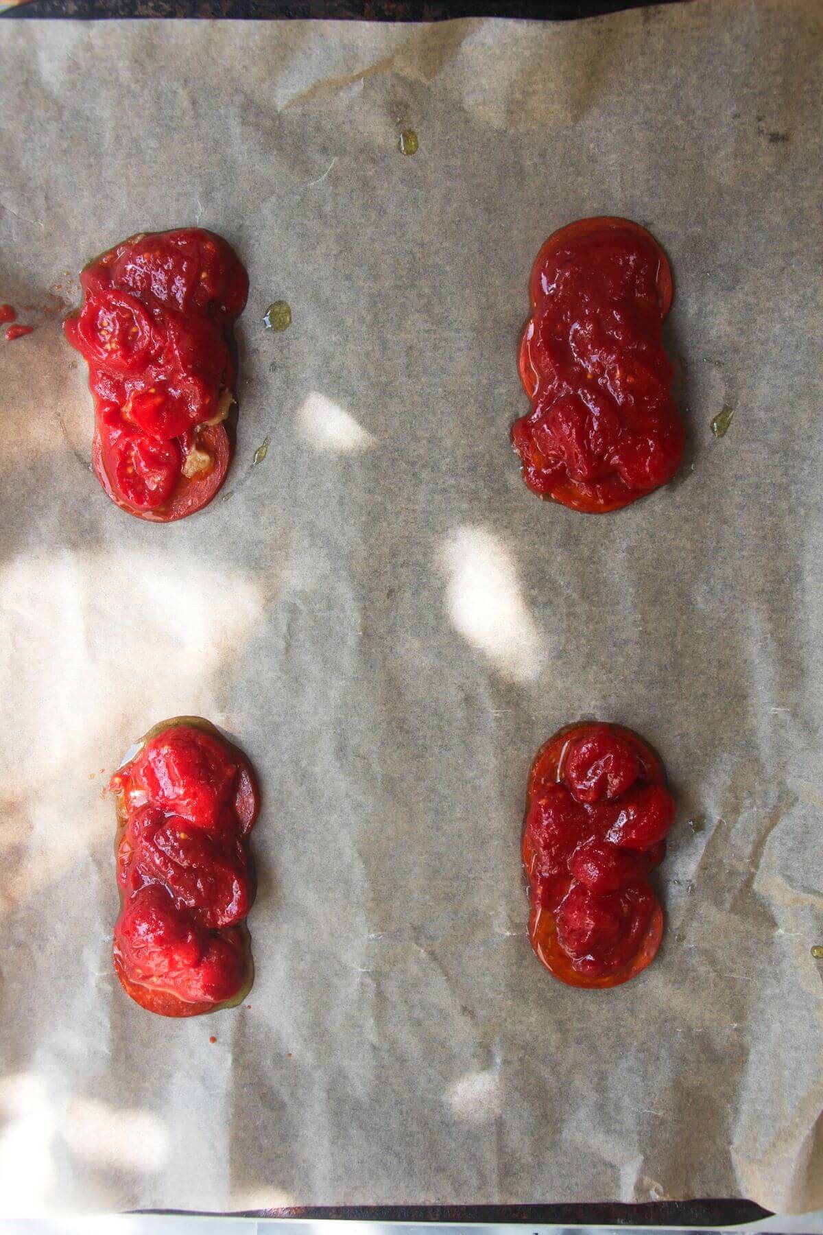 Cherry tomatoes on top of pepperoni on a lined baking tray.