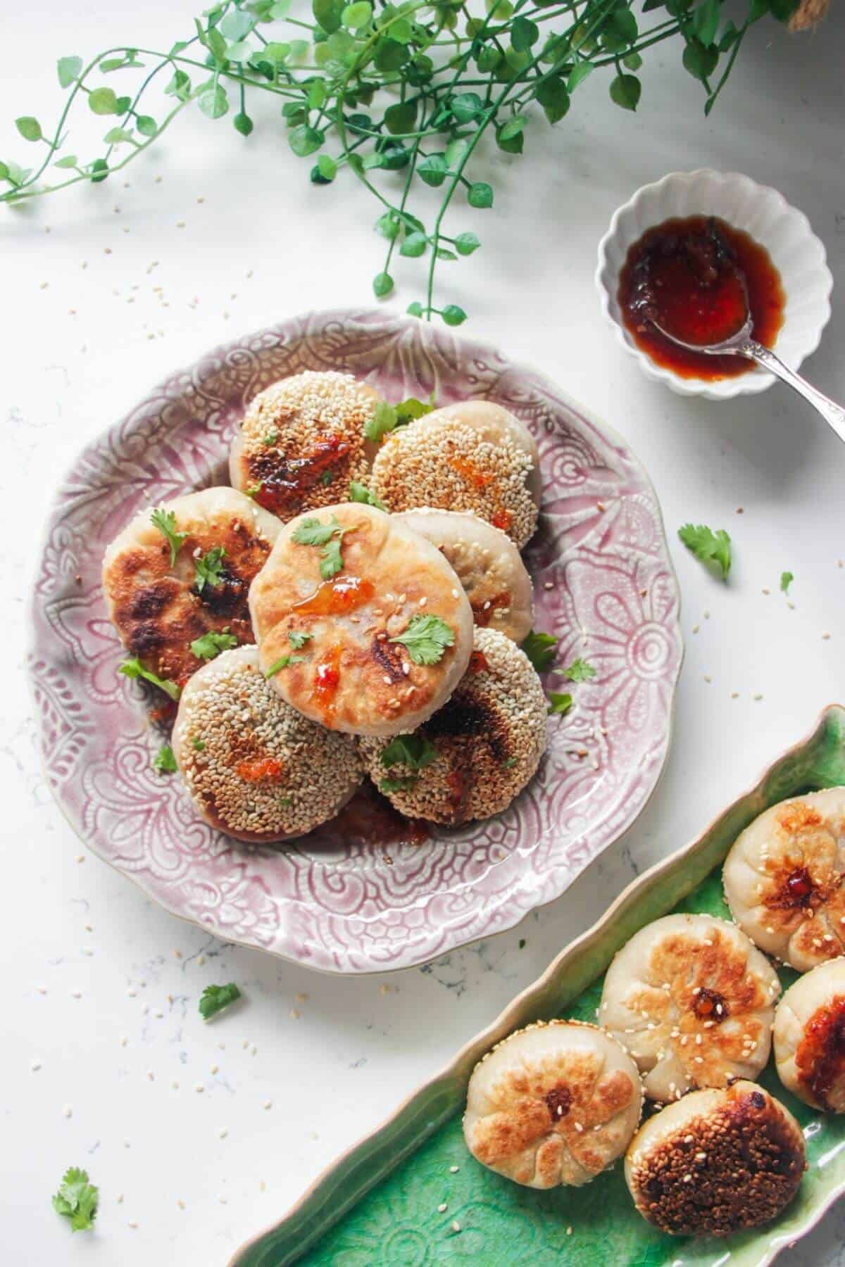 Pan-fried gochujang pizza pockets piled on a small pink plate with more pizza pockets on the side on a green plate.