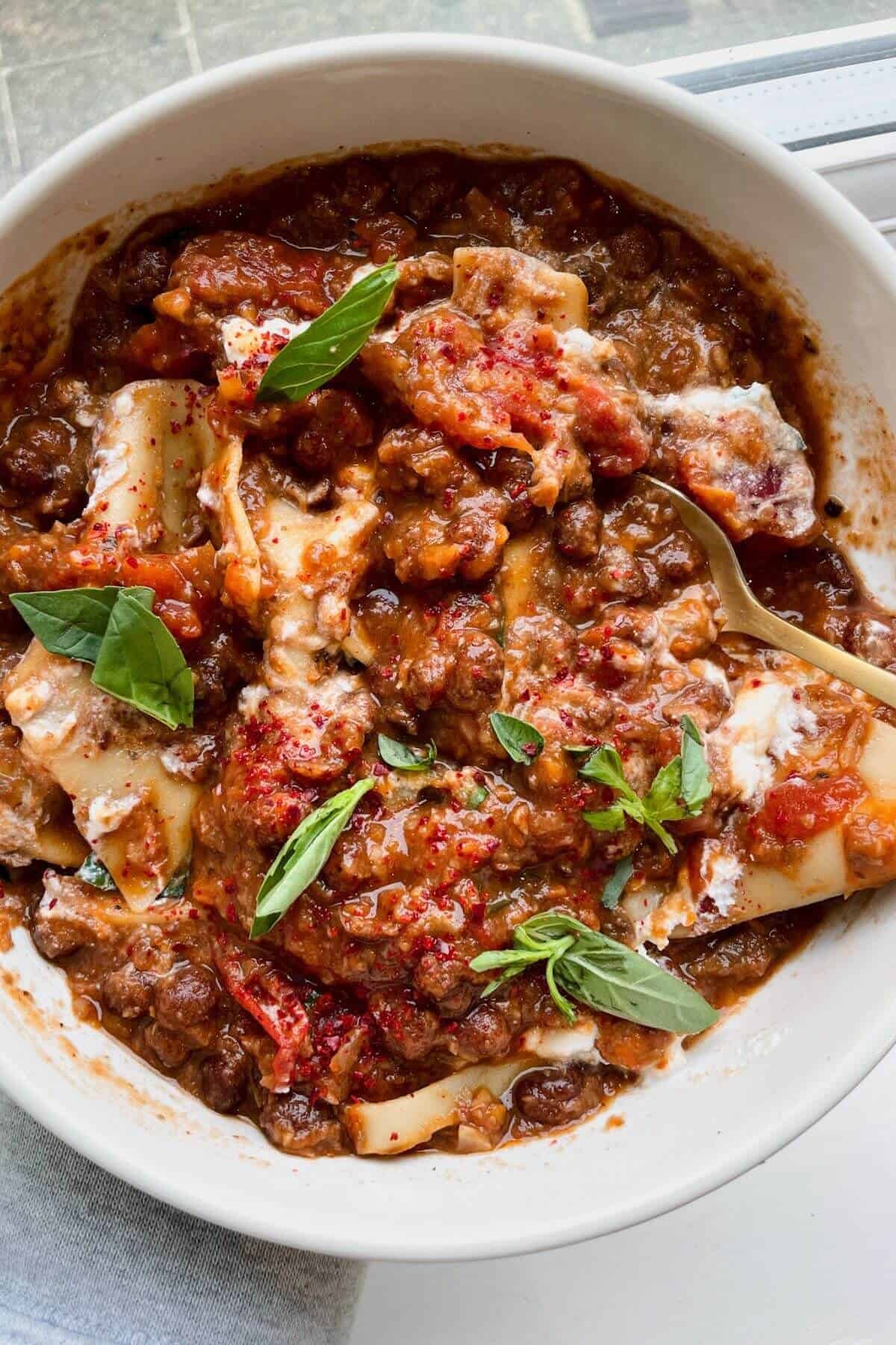 Holding a bowl of lasagna soup with basil and ricotta on top.