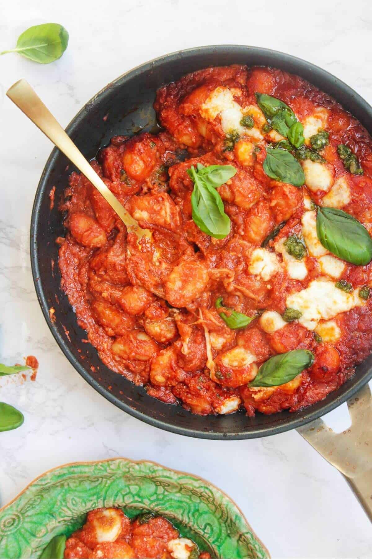 Spoon in a pan of baked gnocchi alla sorrentina in a frying pan, with a bowl of gnocchi on the side.