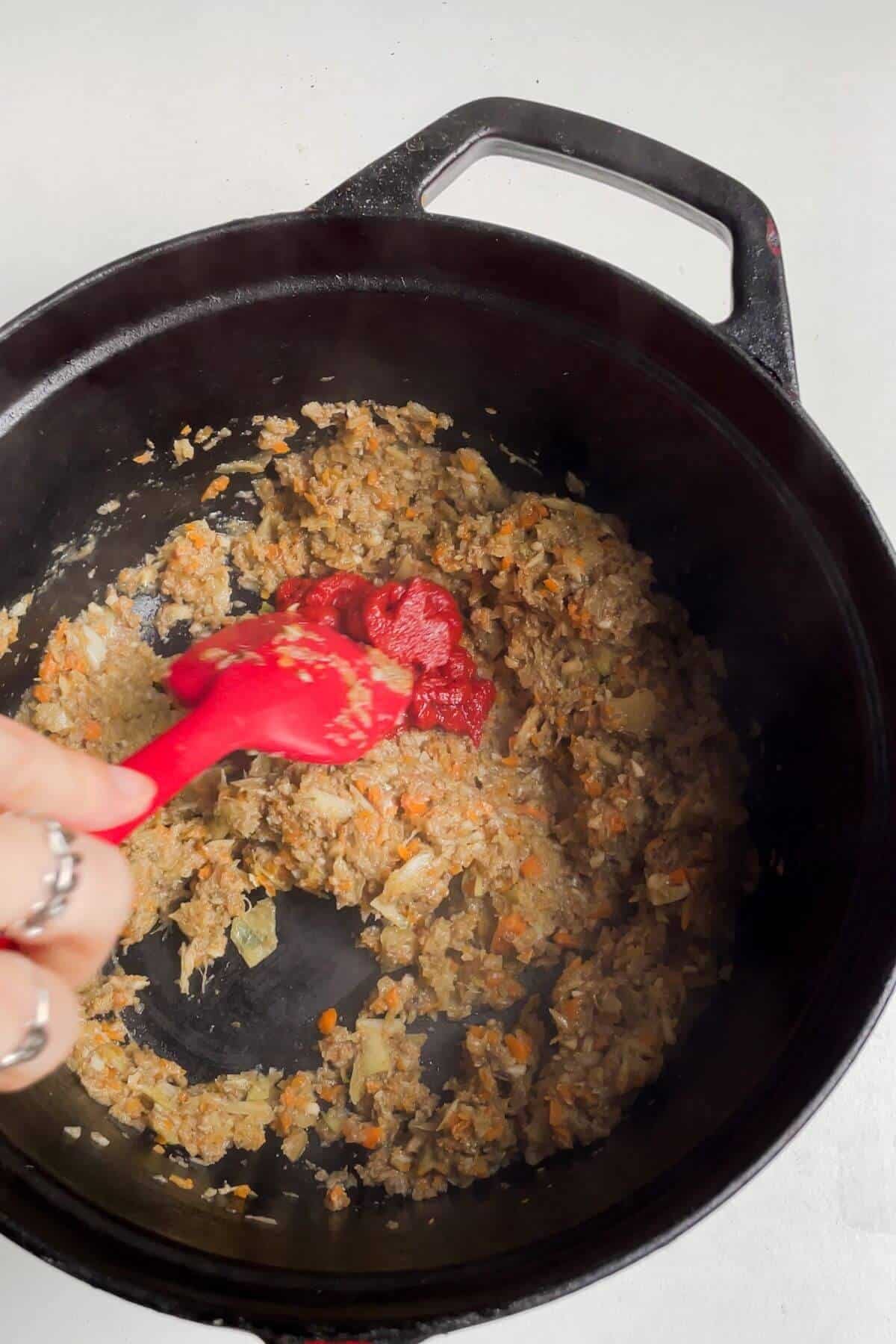 Spatula stirring minced mushroom, garlic, onion, celery and carrot in a large pot.