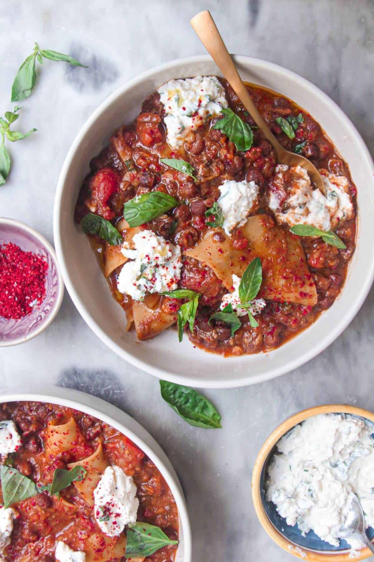 Two bowls of vegetarian lasagna soup, with ricotta on the side.