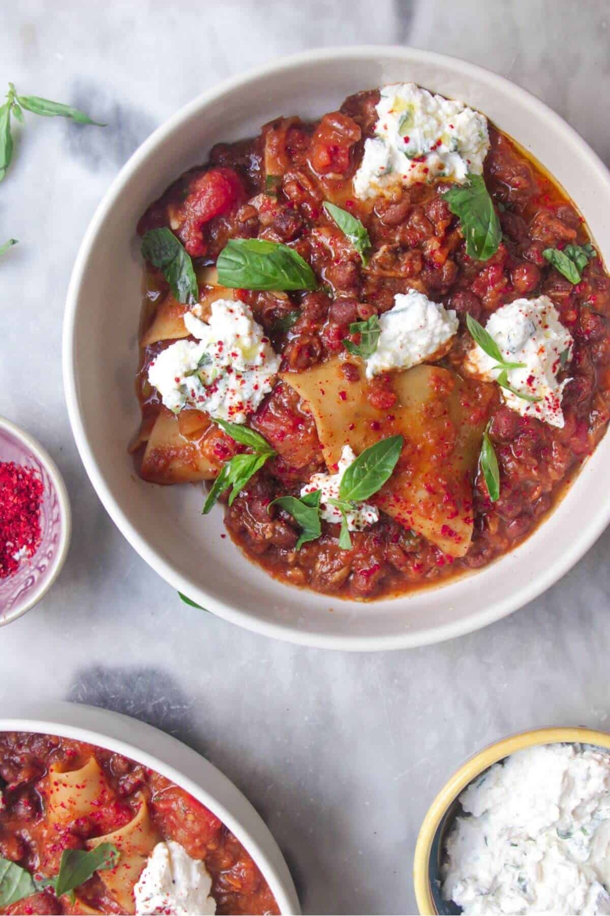Two bowls of vegetarian lasagna soup, with ricotta on the side.