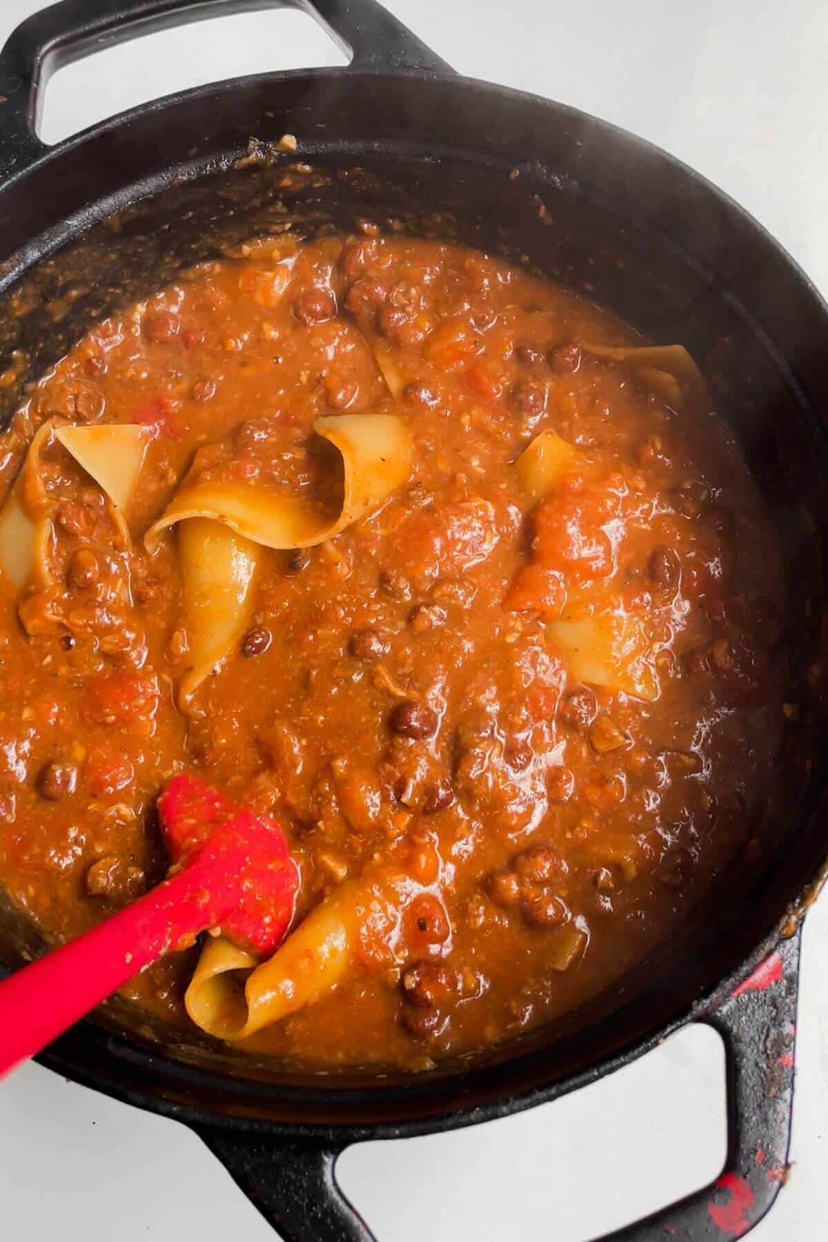 Spatula stirring lasagna sheets through soup in a large pot.