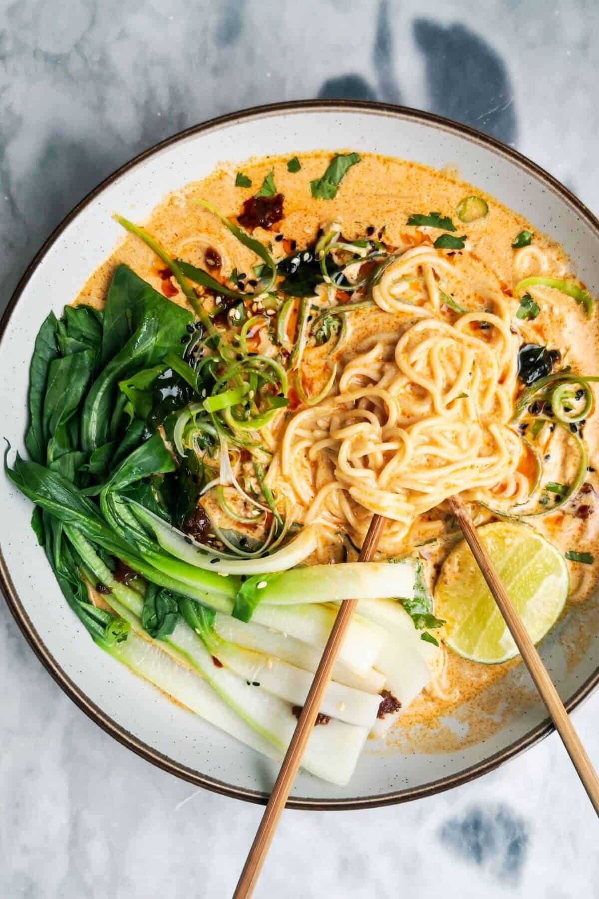 Quick spicy coconut noodles in a bowl on a grey marble background with chopsticks in the bowl.