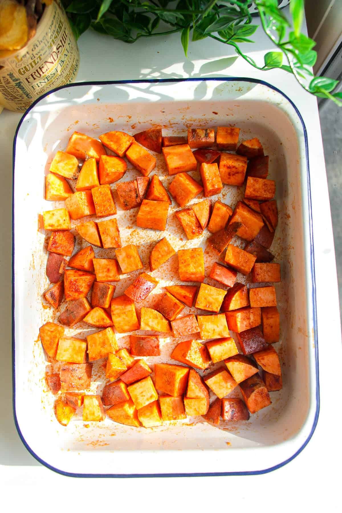 Diced sweet potato tossed with spices in an oven tray.