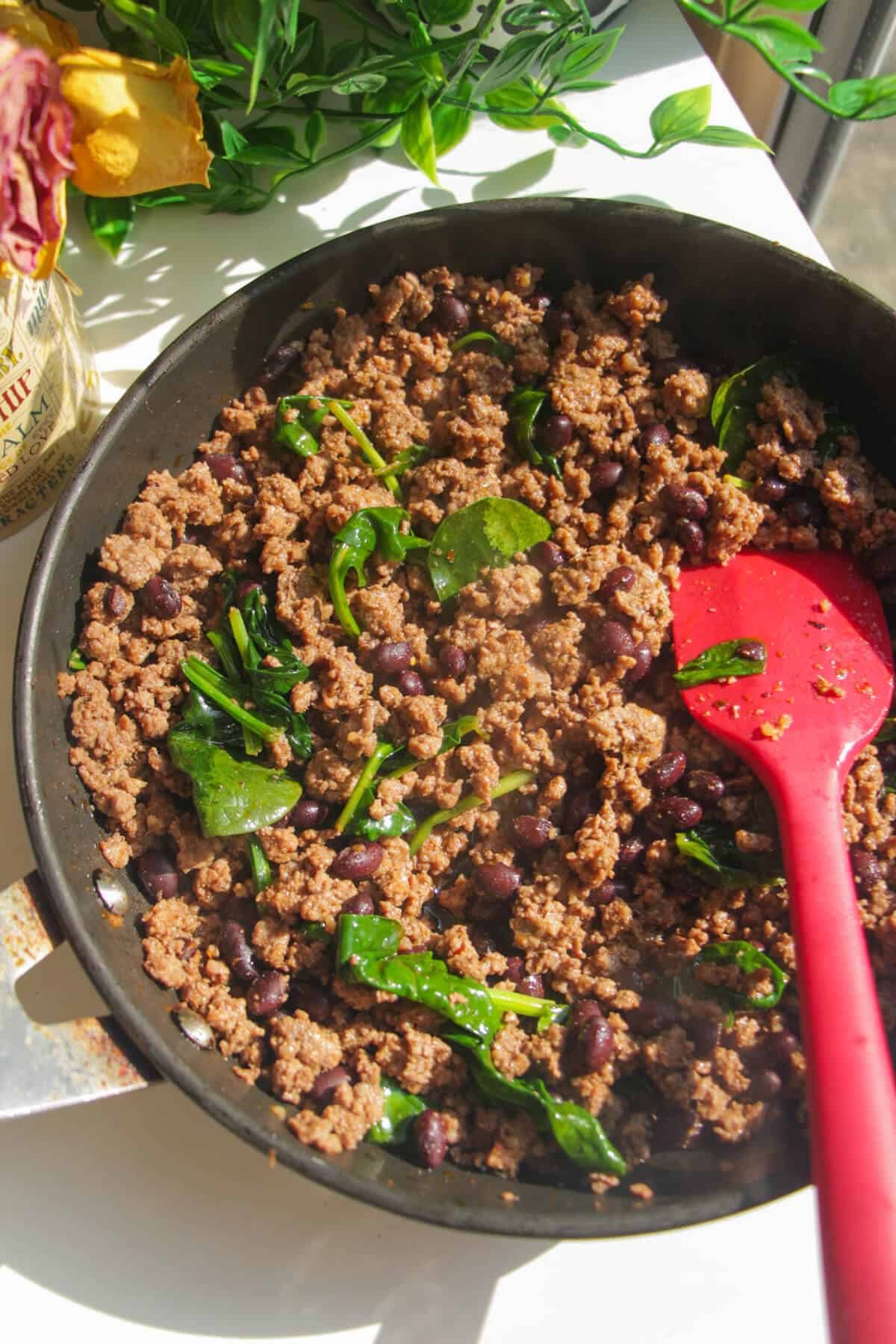Spinach and black beans mixed through taco ground beef in a pan.