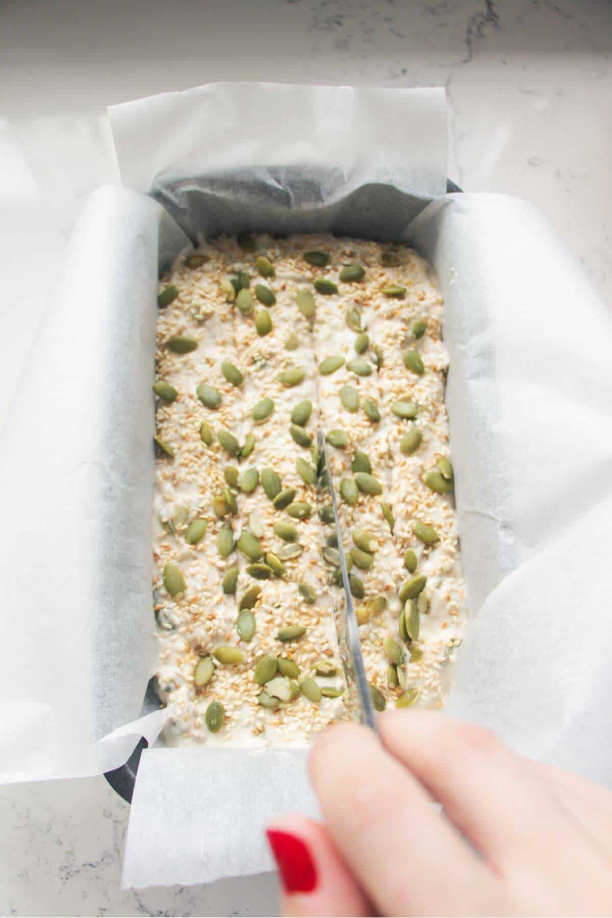 A silver knife slicing through the top of Vogel's style bread dough in an oven tin.