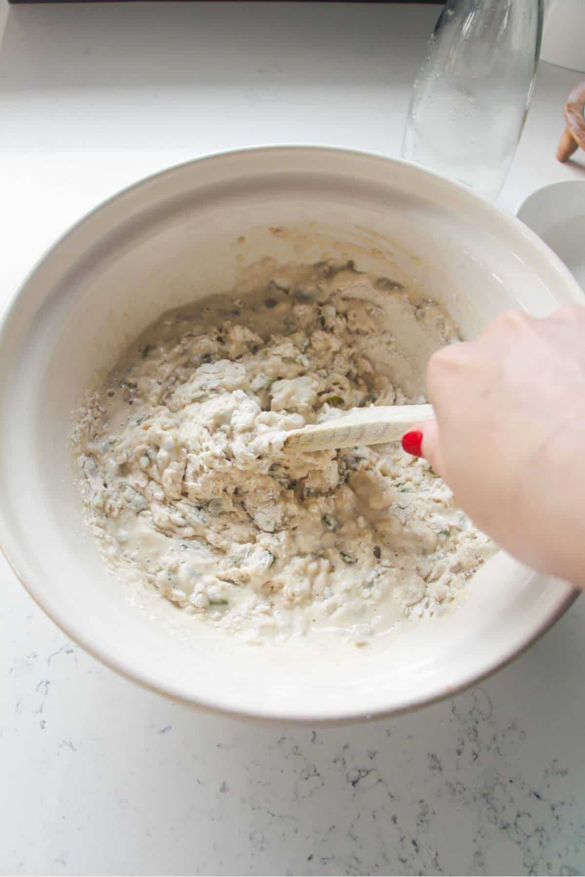A hand holding a wooden spoon to mix Vogel's style bread dough.