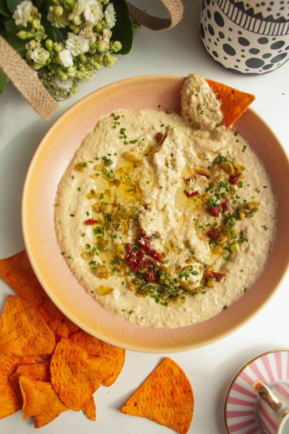 Whipped cottage cheese dip in a pink bowl with flowers on the side and a tortilla chip in the bowl.
