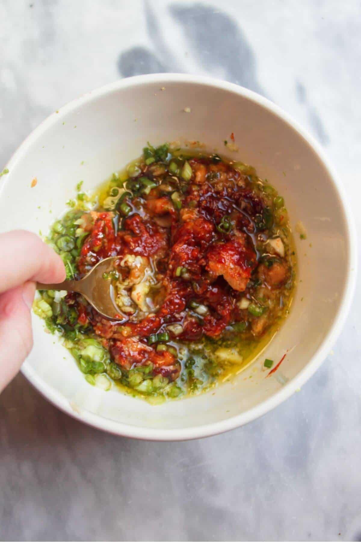 Small gold spoon mixing miso gochujang marinade in a small white bowl.