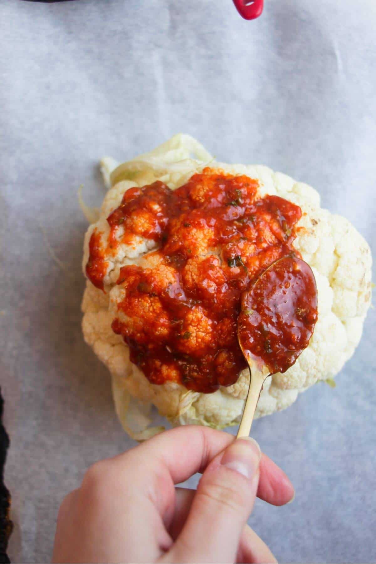 Spooning miso gochujang marinade on top of cauliflower on a baking paper lined tray.
