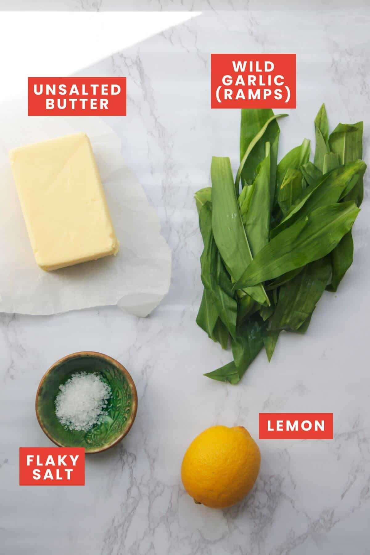 Ingredients for wild garlic butter laid out on a white marble background and labelled.