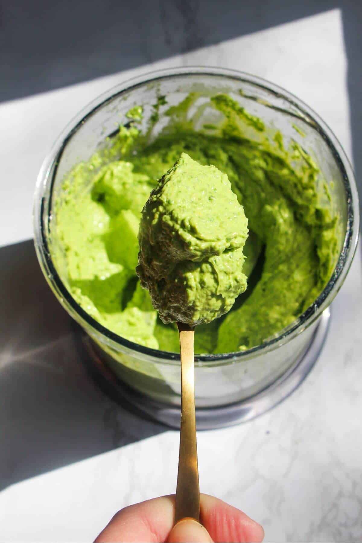 Hand holding up a small gold spoon with wild garlic butter on it.