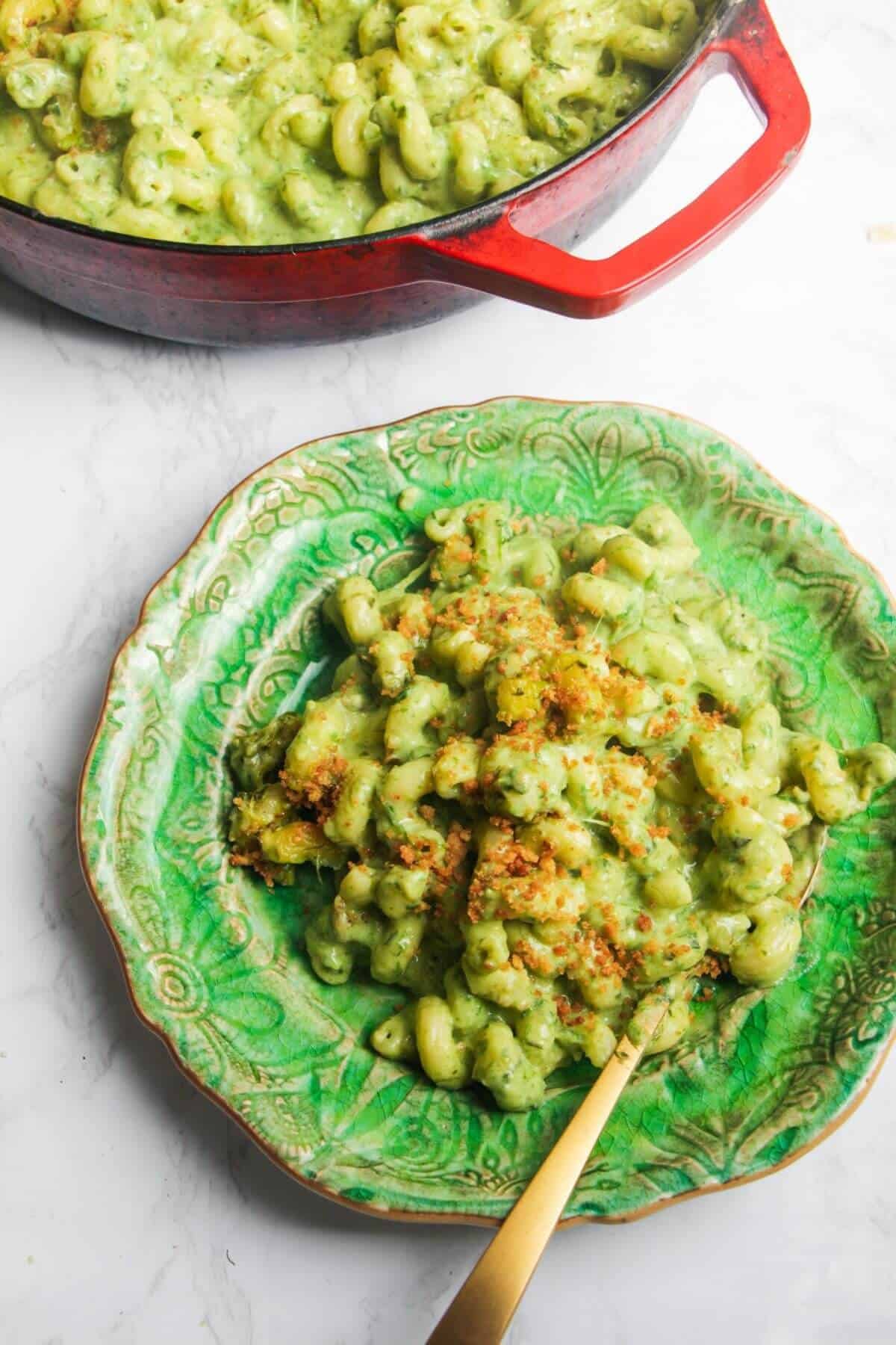Gooey green wild garlic mac and cheese on a small green plate with more mac and cheese in the background.