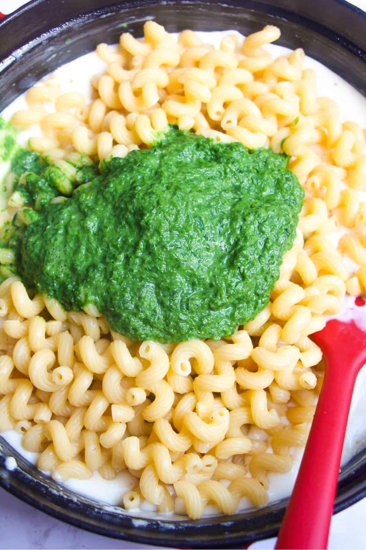 Cooked pasta and wild garlic puree added to cheesy bechamel sauce in a large black pan.