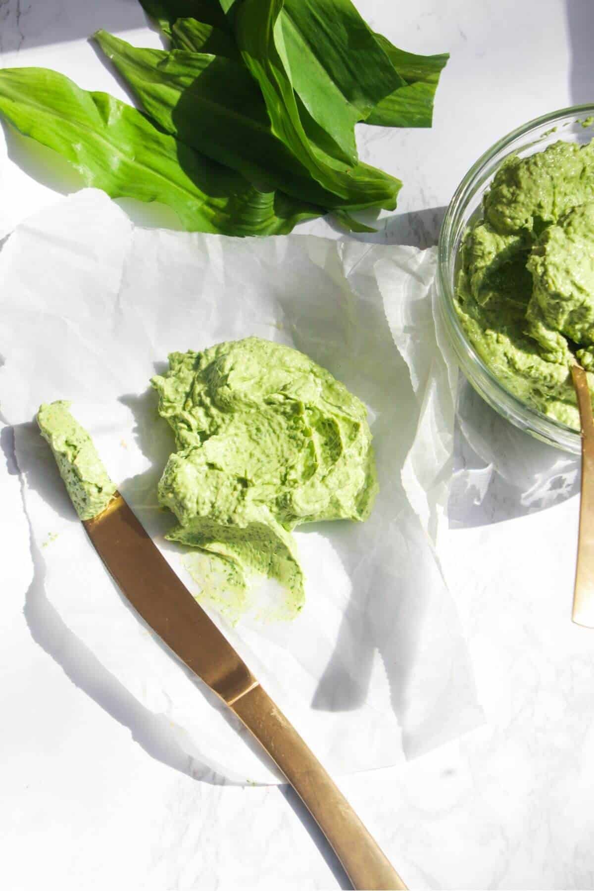 Wild garlic butter on a piece of baking paper with more wild garlic butter in a small glass bowl, with a god knife on the side.