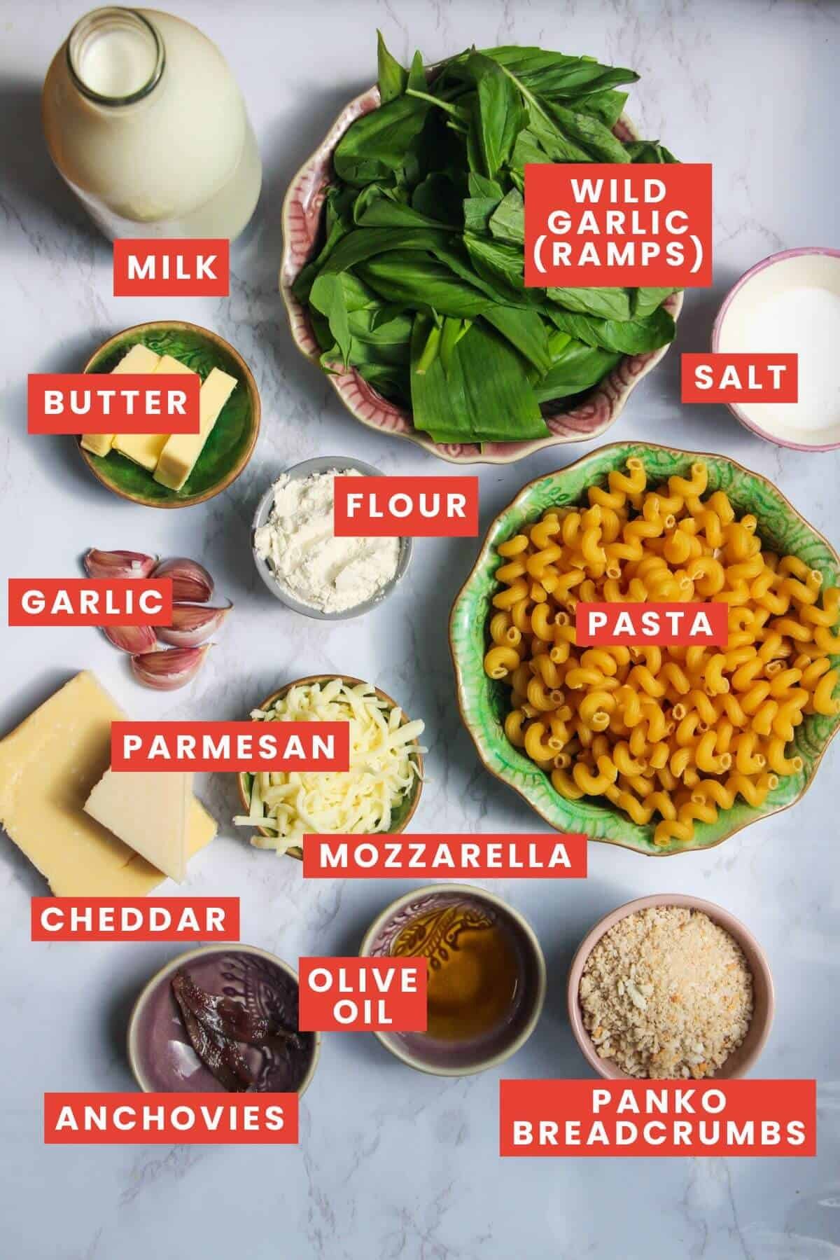 Ingredients for wild garlic mac and cheese laid out on a white marble background and labelled.