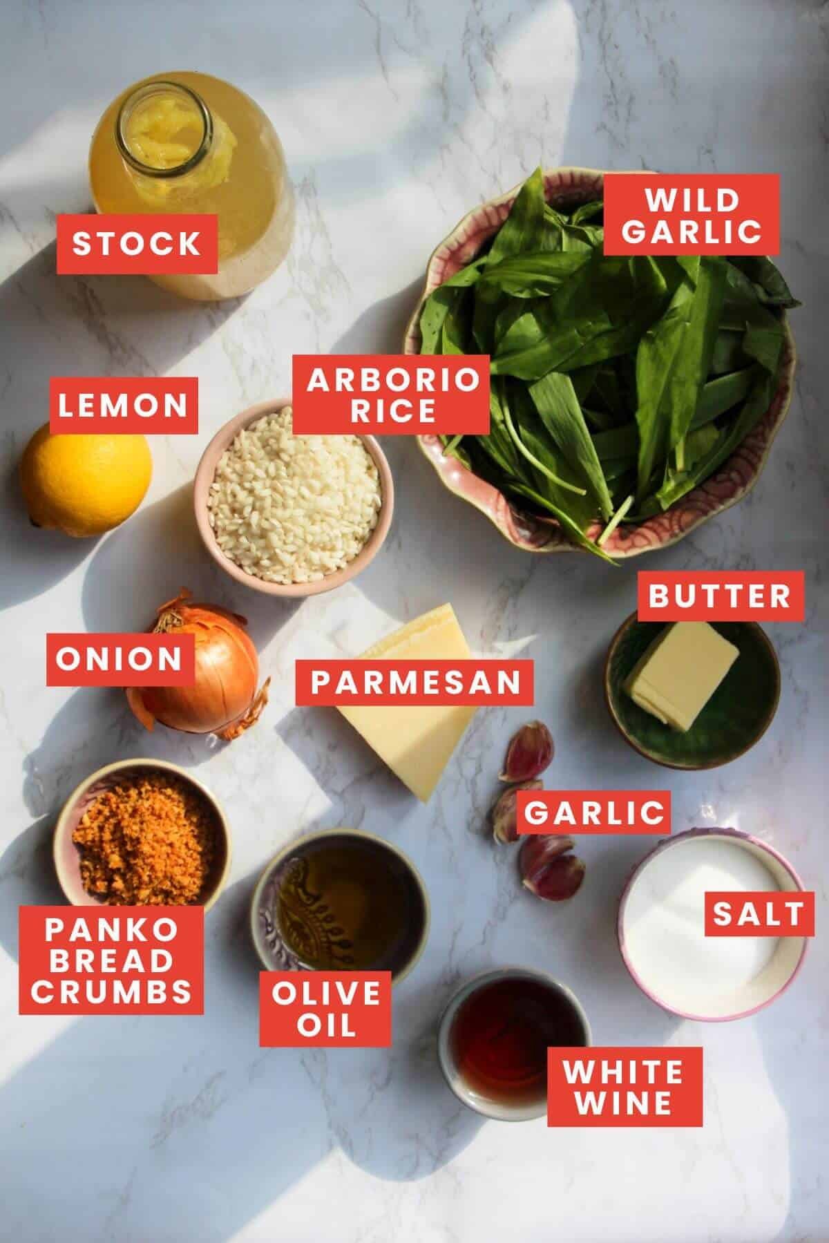 Wild garlic risotto ingredients laid out on a white marble background and labelled.