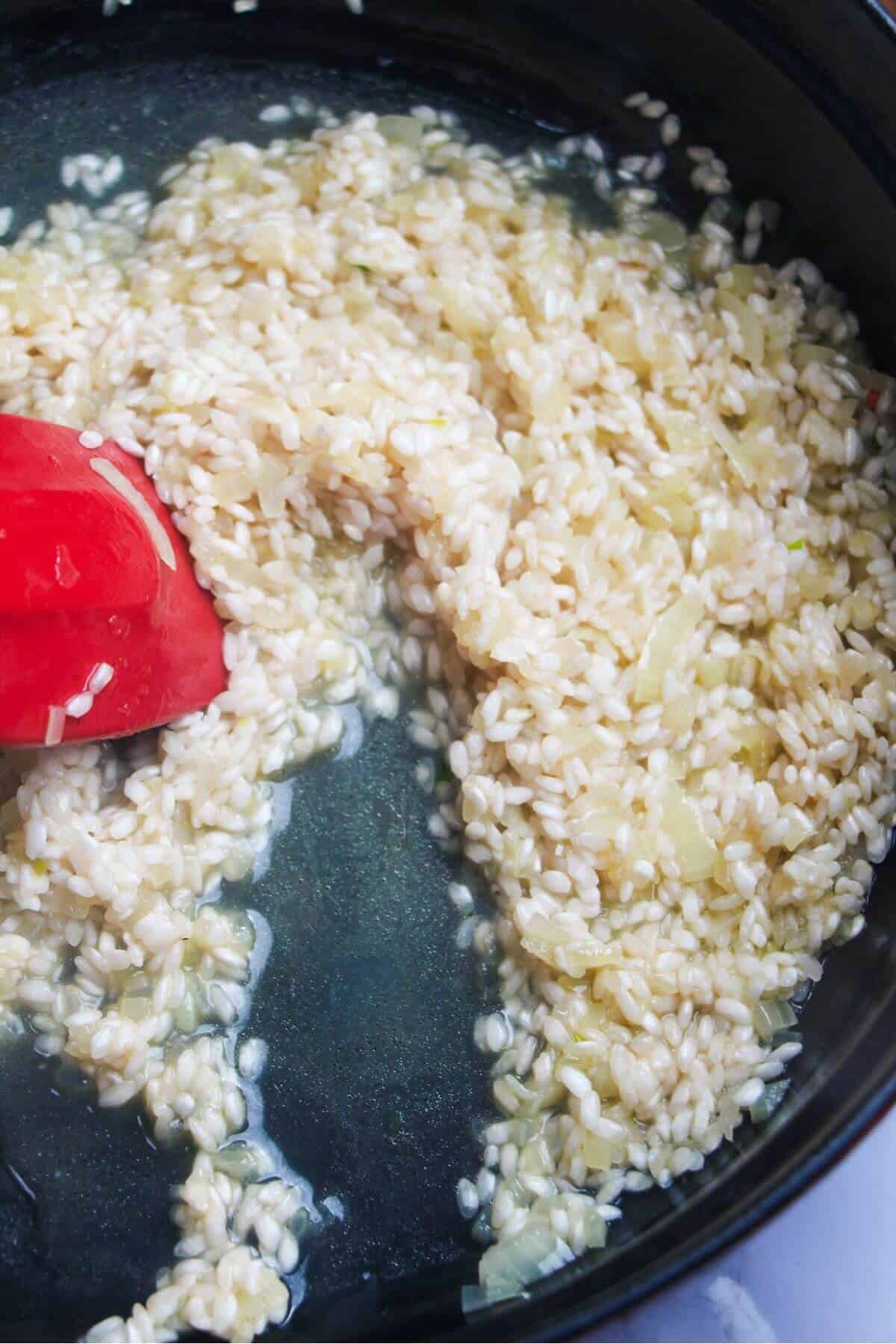 Red spatula stirring risotto in a large black skillet.