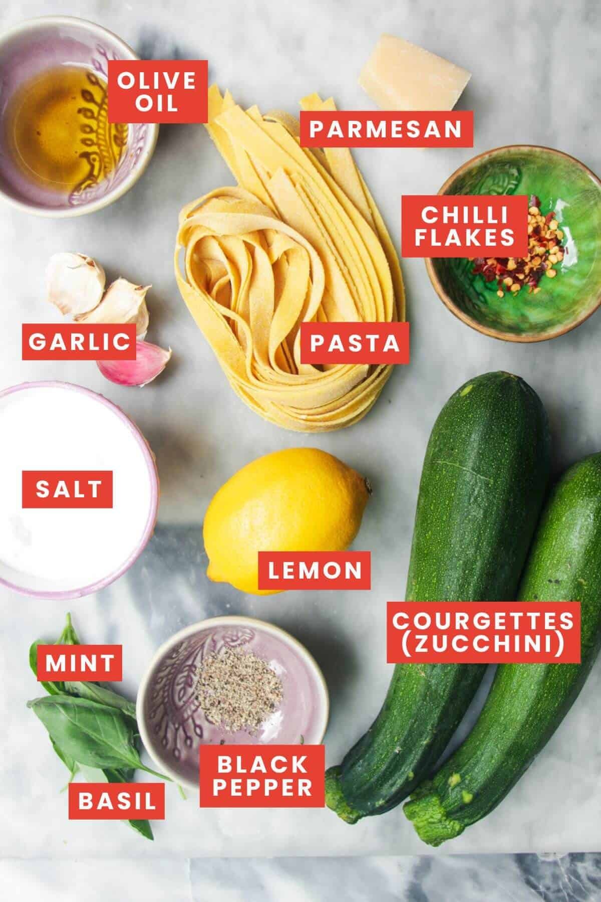 Zucchini pasta ingredients laid out on a grey marble background and labelled.