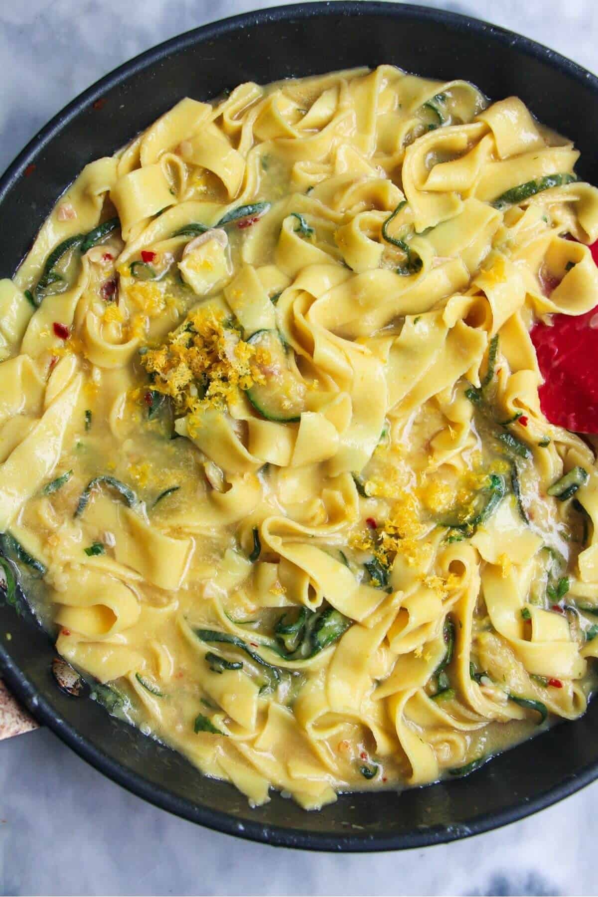 Courgette tossed through cooked fettuccine in a small black pan.
