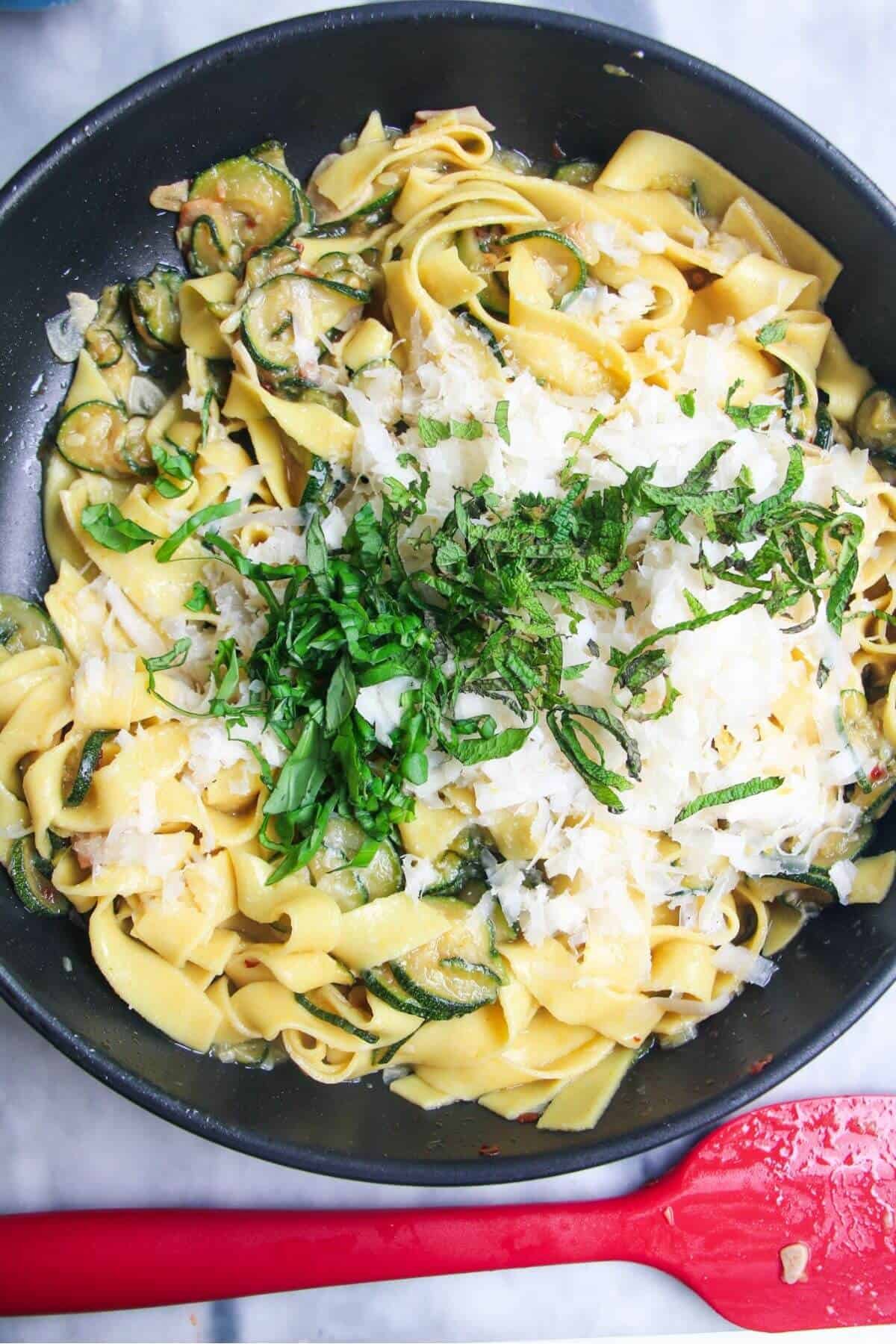Grated parmesan and mint leaves on top of fettuccine in a small black pan.