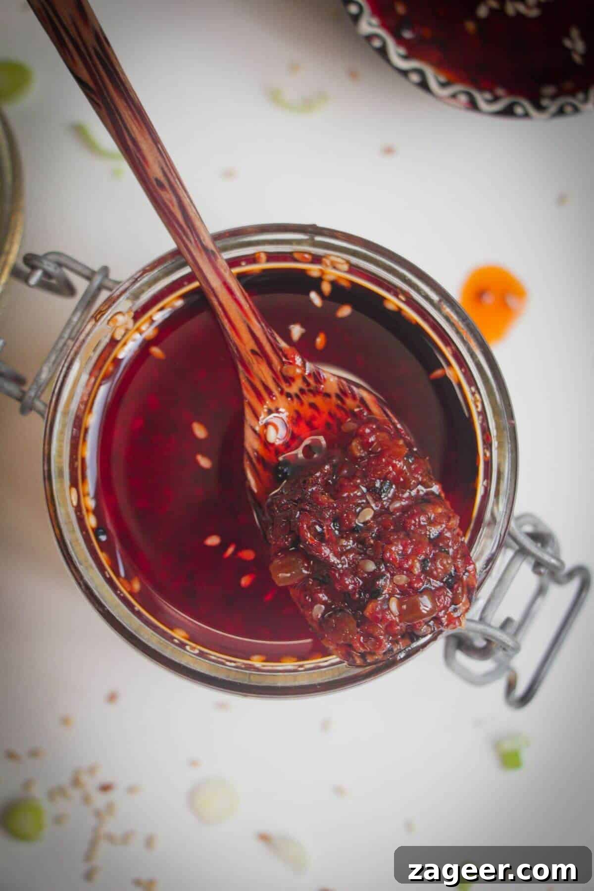 Wooden spoon in a jar of chili oil, highlighting its rich red color and inviting texture.