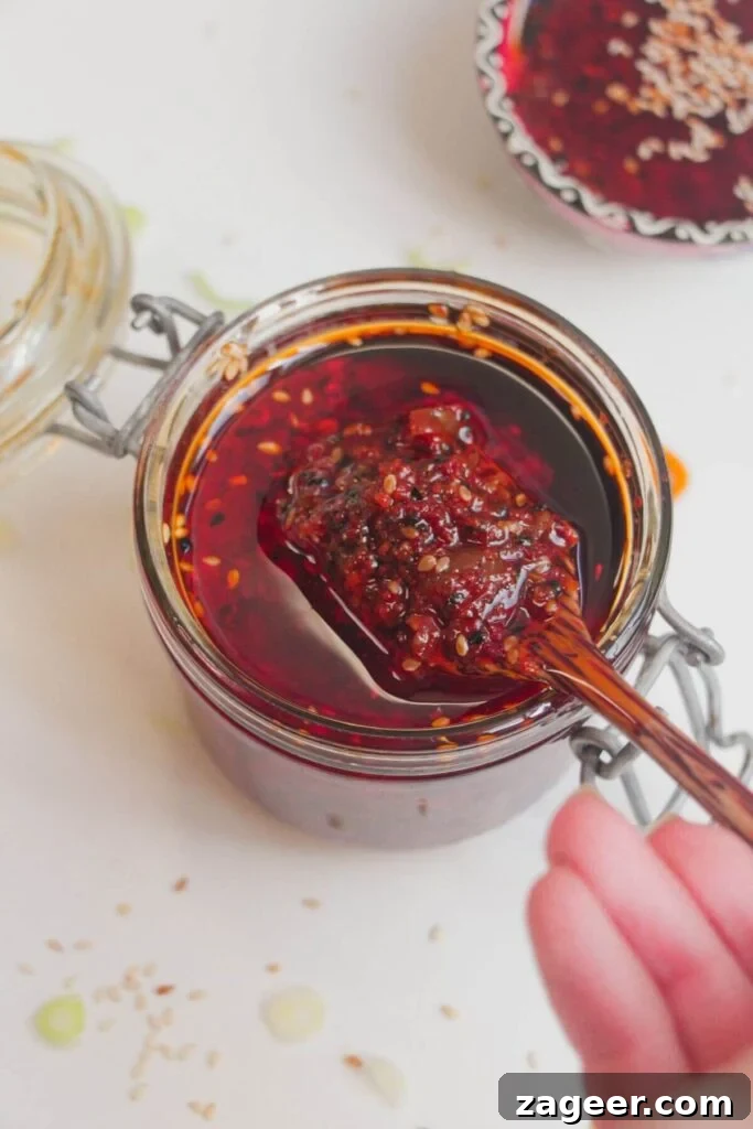Hand holding a wooden spoon with chili oil on it, showcasing its texture.