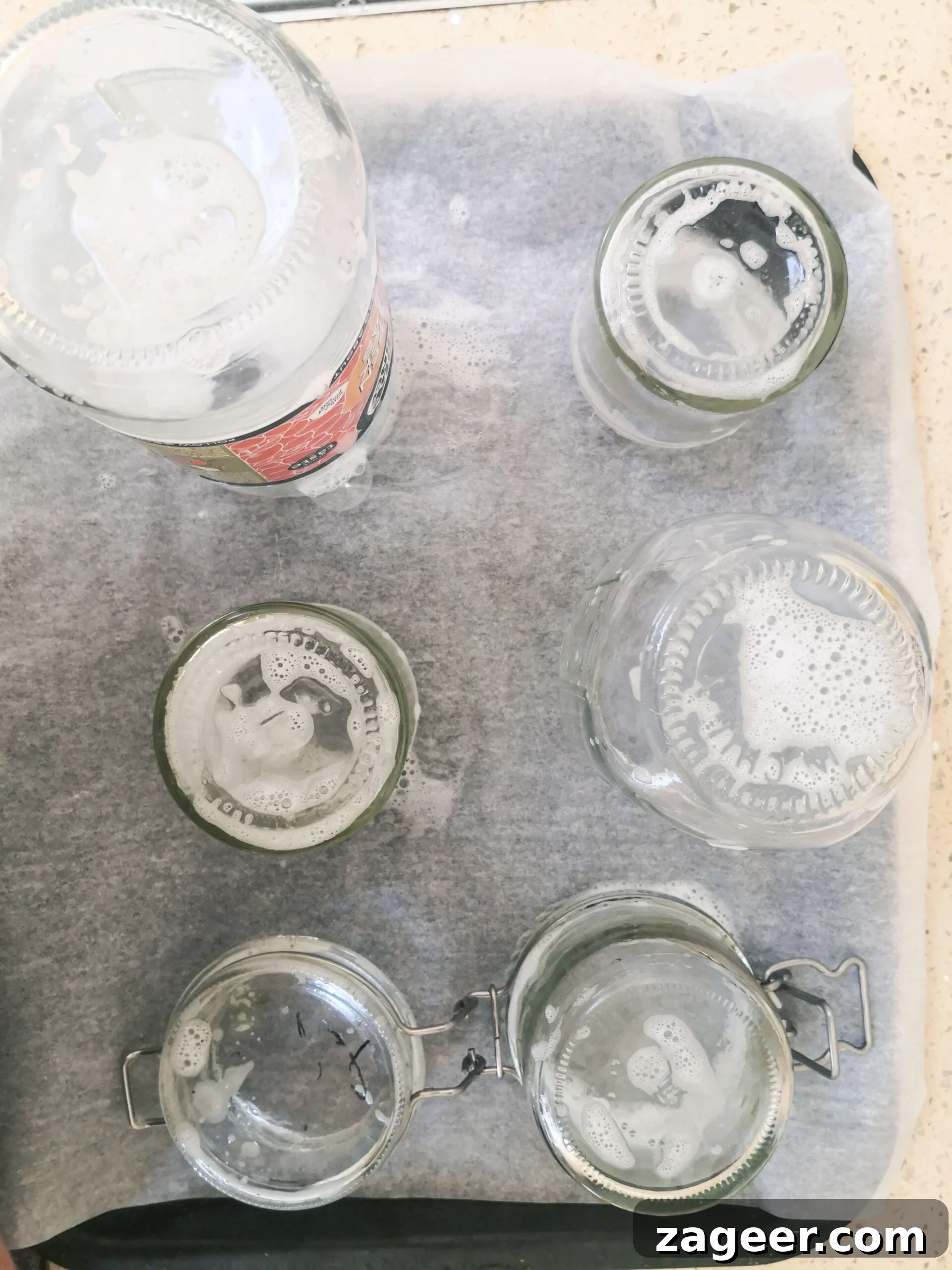 Soapy glass jars standing upright on a lined oven tray, ready for sterilization.