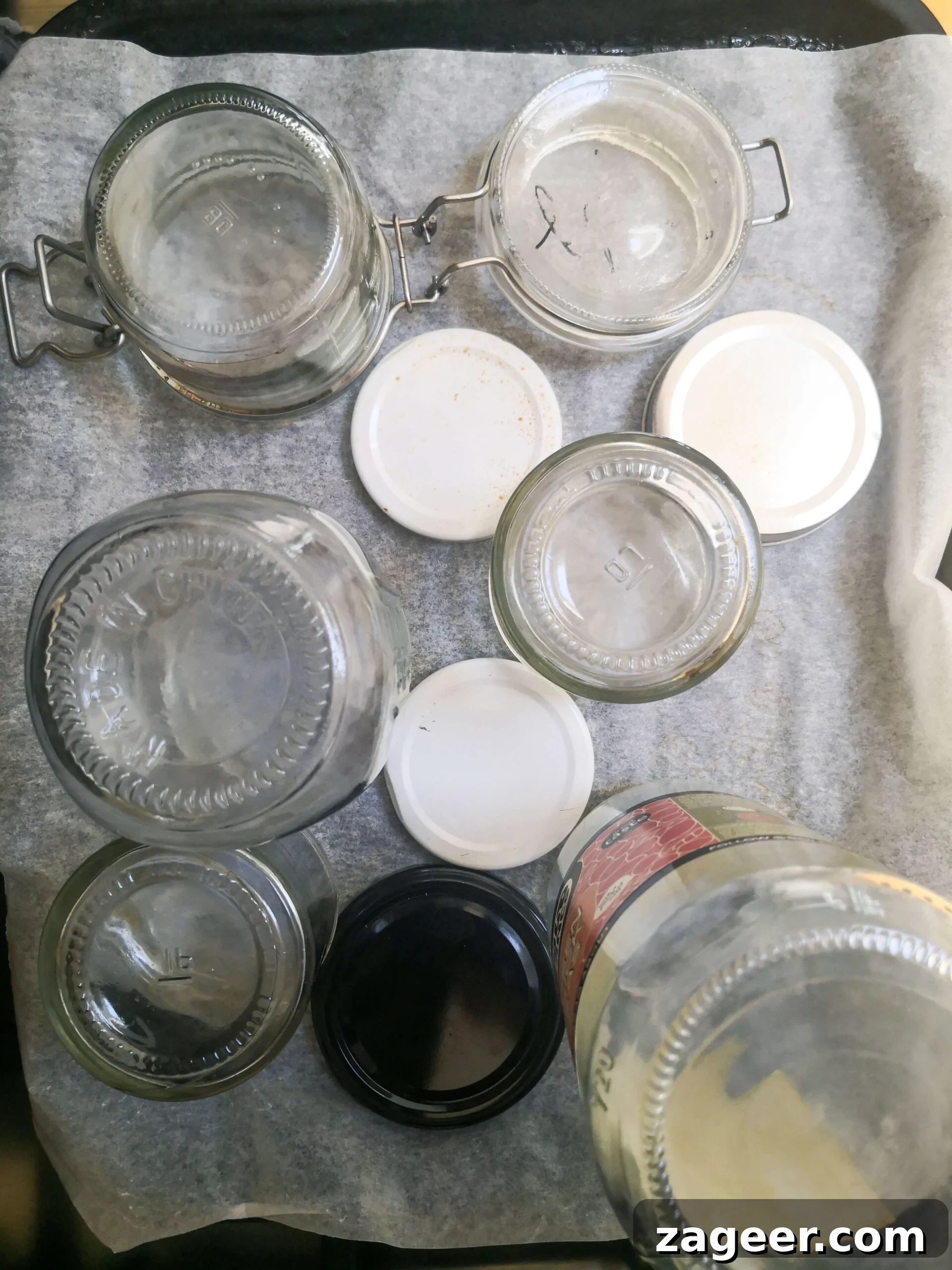 Sterilized glass jars standing upside down on a lined oven tray to cool.