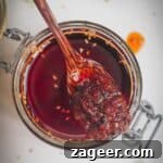 Wooden spoon in a jar of chili oil, invitingly rich in color.