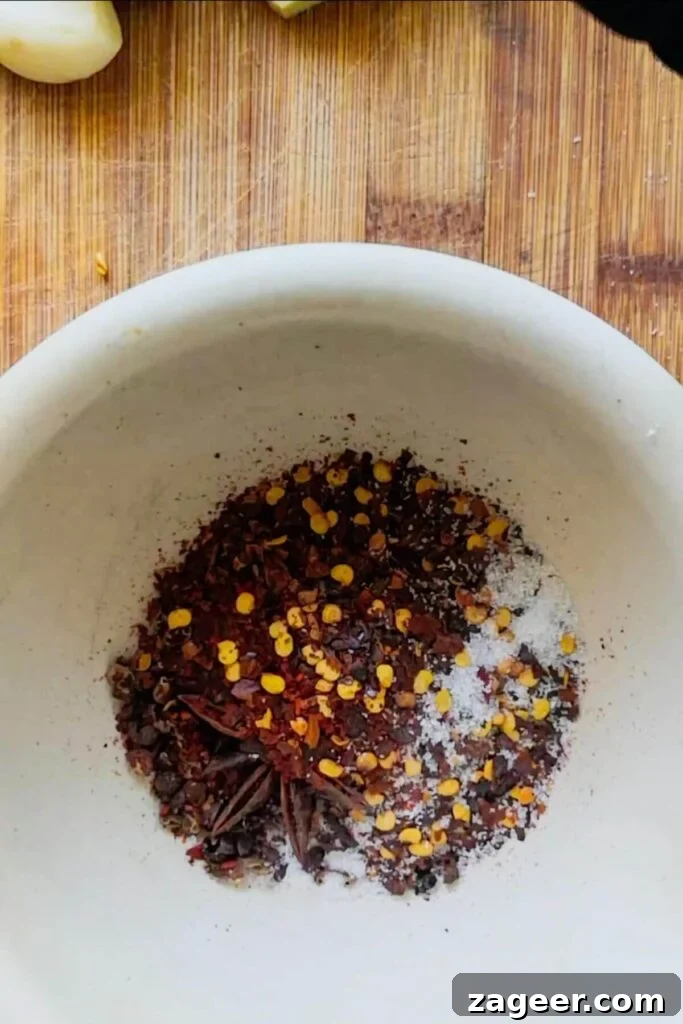 Chili flakes, star anise, Szechuan peppercorns, and salt in a white pestle and mortar.