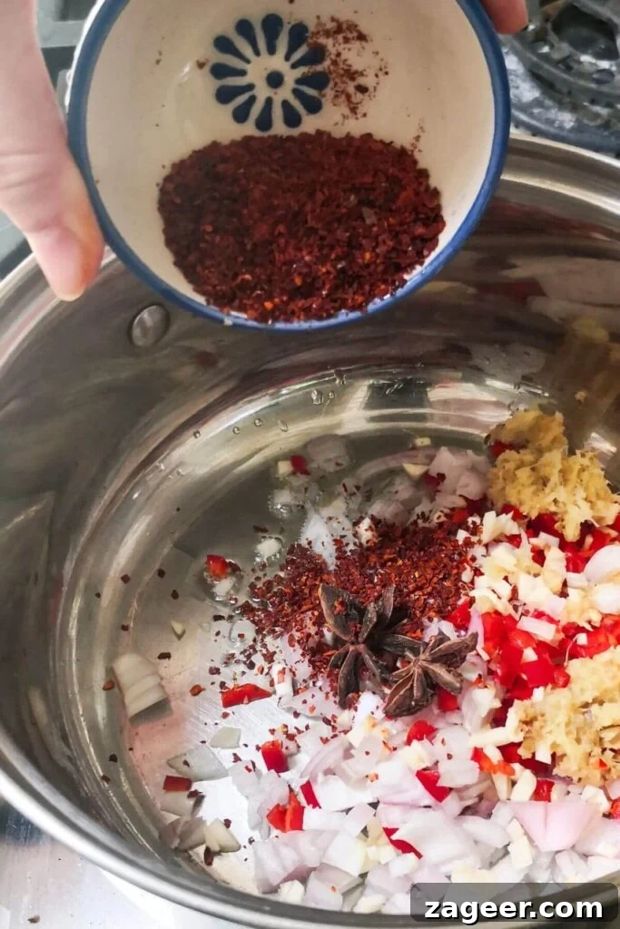 Spices being added to small silver pot with other chili oil ingredients.