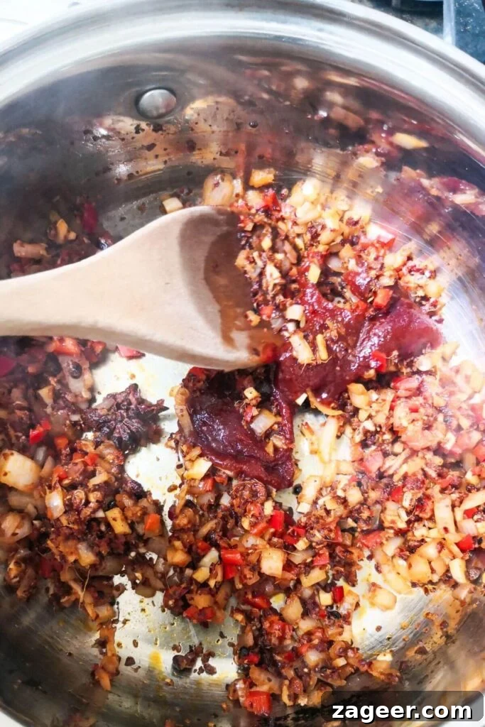 Gochujang paste being stirred into chili oil ingredients in a small silver pot.