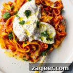 Spicy nduja pasta with torn burrata ball on top with basil on a white plate with a gold fork.