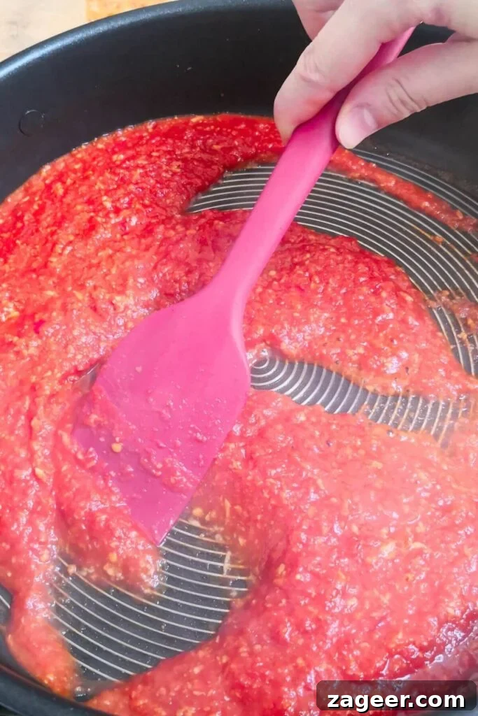 Quick Spicy Nduja Pasta with Creamy Burrata 5 Red spatula stirring nduja tomato sauce in a large black pan, showing the rich color.