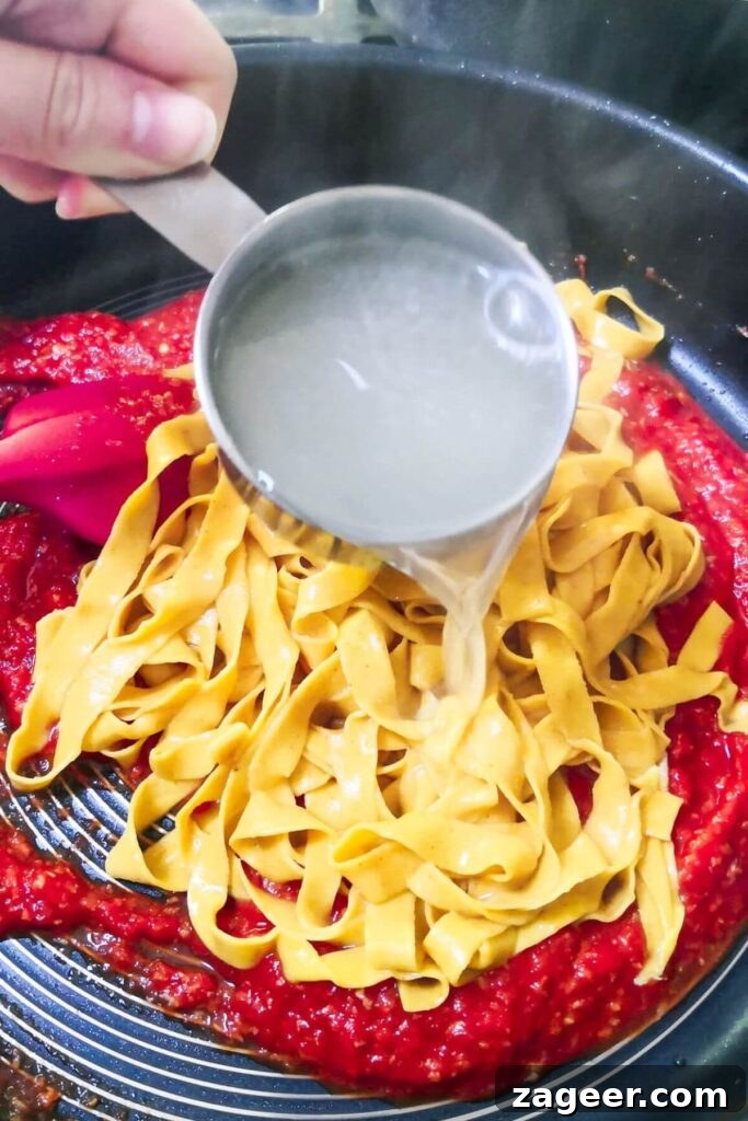 Quick Spicy Nduja Pasta with Creamy Burrata 6 A small cup of pasta water being added to pasta and nduja pasta sauce in a large pan, showing steam.