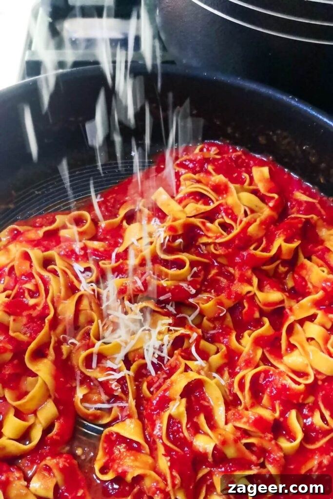 Quick Spicy Nduja Pasta with Creamy Burrata 7 Grated parmesan being scattered on top of nduja pasta in a large pan, ready for tossing.