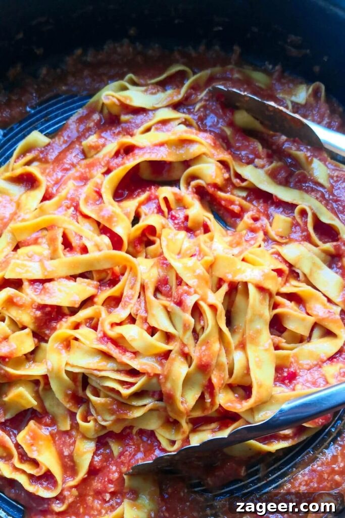 Quick Spicy Nduja Pasta with Creamy Burrata 8 Nduja pasta being tossed through sauce with large silver tongs in a pan, ensuring even coating.