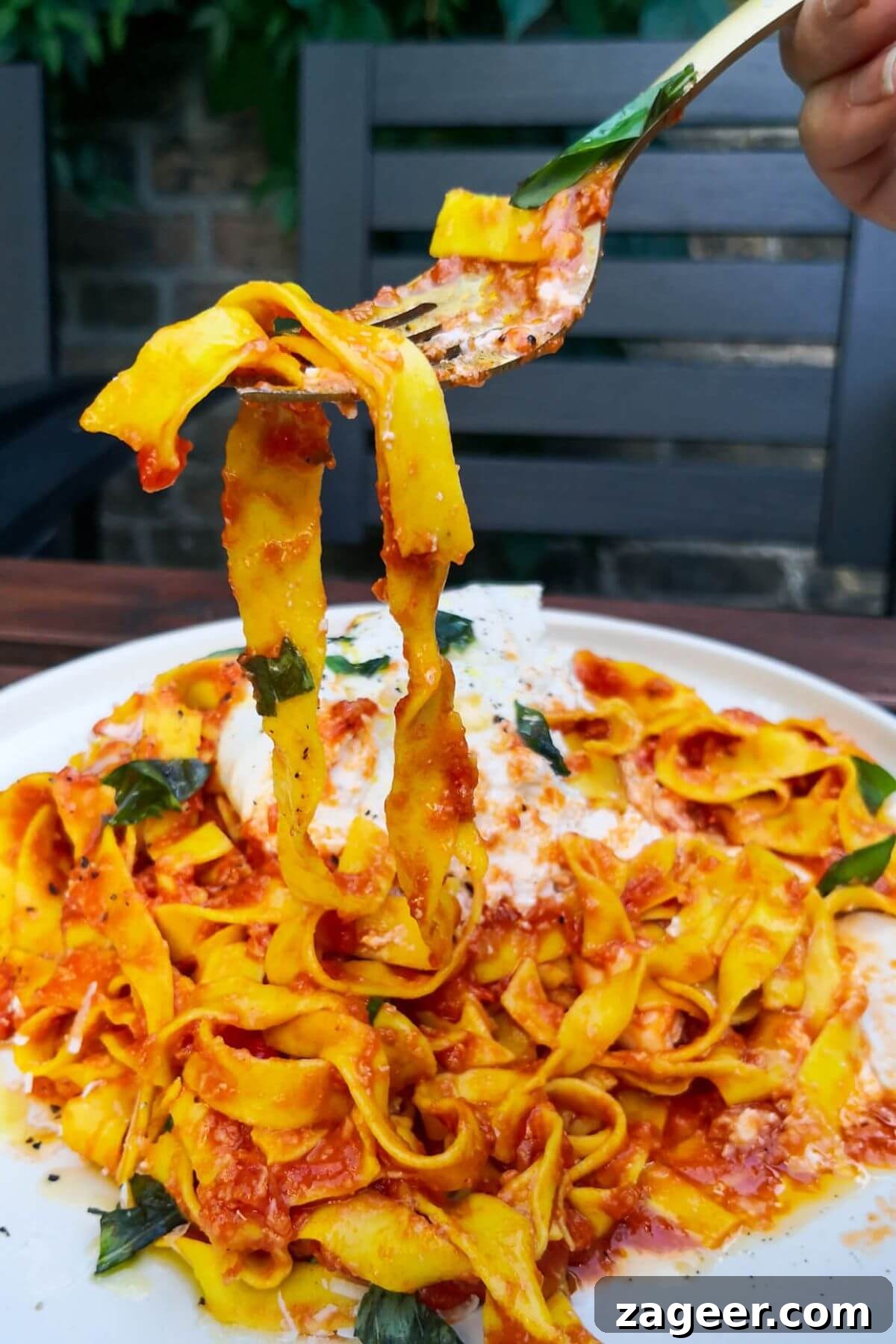 Quick Spicy Nduja Pasta with Creamy Burrata 10 Nduja pasta being pulled up by a fork from a large white plate of pasta, showing its glossy sauce.