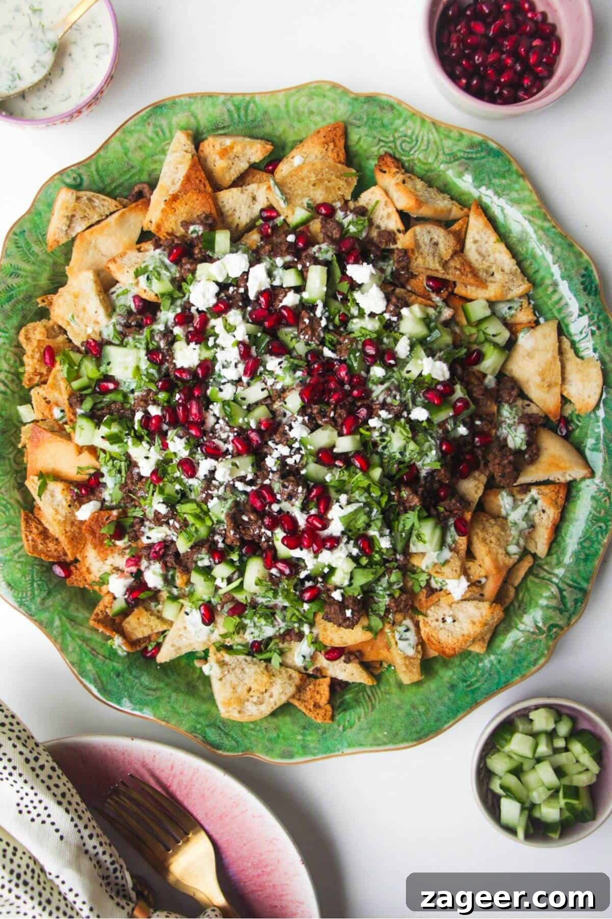 Sticky Beef Fatteh Middle Eastern Layered Nachos 2 A vibrant platter of Middle Eastern style nachos, or sticky beef fatteh, adorned with fresh cucumber slices and a rich tahini drizzle, inviting guests to dig in.