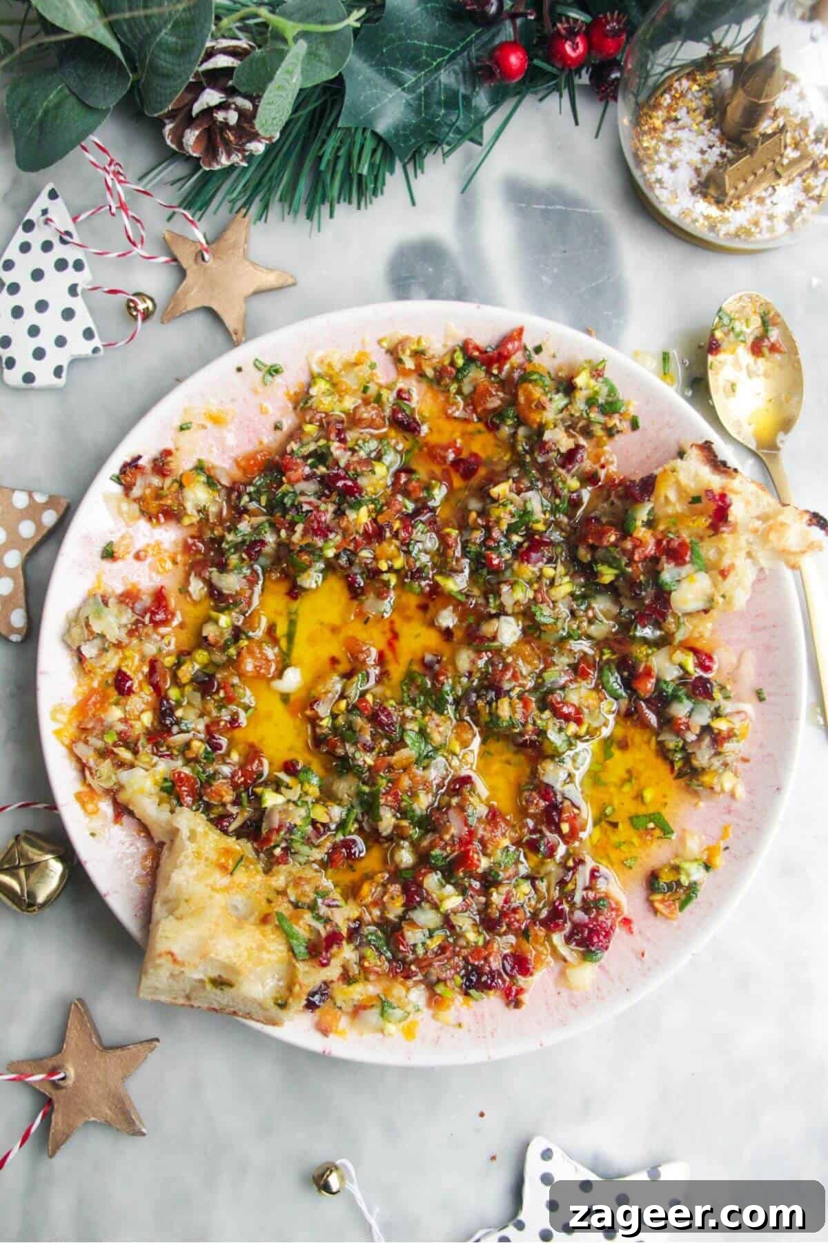 Gourmet Holiday Bread Dipping Blend 2 A small pink plate filled with festive dipping oil, garnished with herbs and dried fruits, resting on a grey surface.