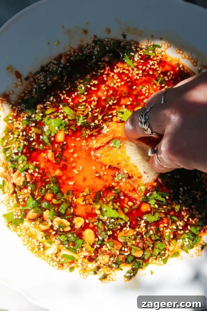 Gourmet Holiday Bread Dipping Blend 11 A hand dipping bread into a luscious sweet chili dipping oil, showcasing its vibrant color.