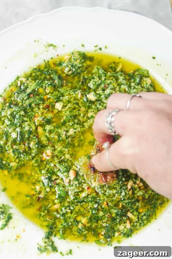 Gourmet Holiday Bread Dipping Blend 8 A hand sweeping a piece of bread through a vibrant green pesto dipping oil in a scalloped white plate.