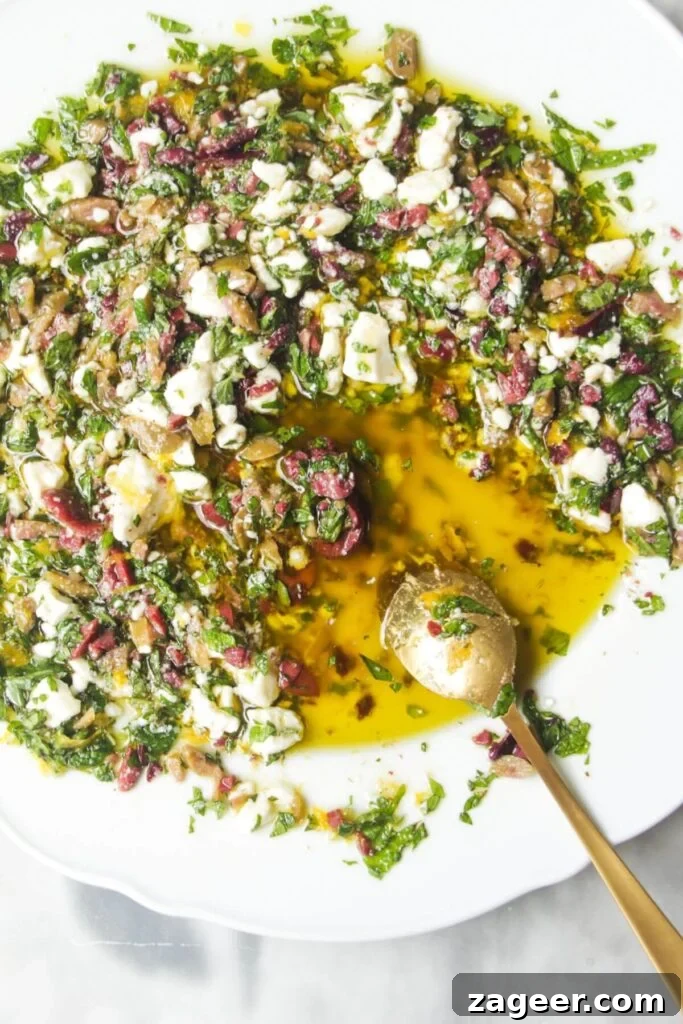 Gourmet Holiday Bread Dipping Blend 10 A small gold spoon resting in a Greek-style bread dipping oil, rich with feta and olives, on a white plate.