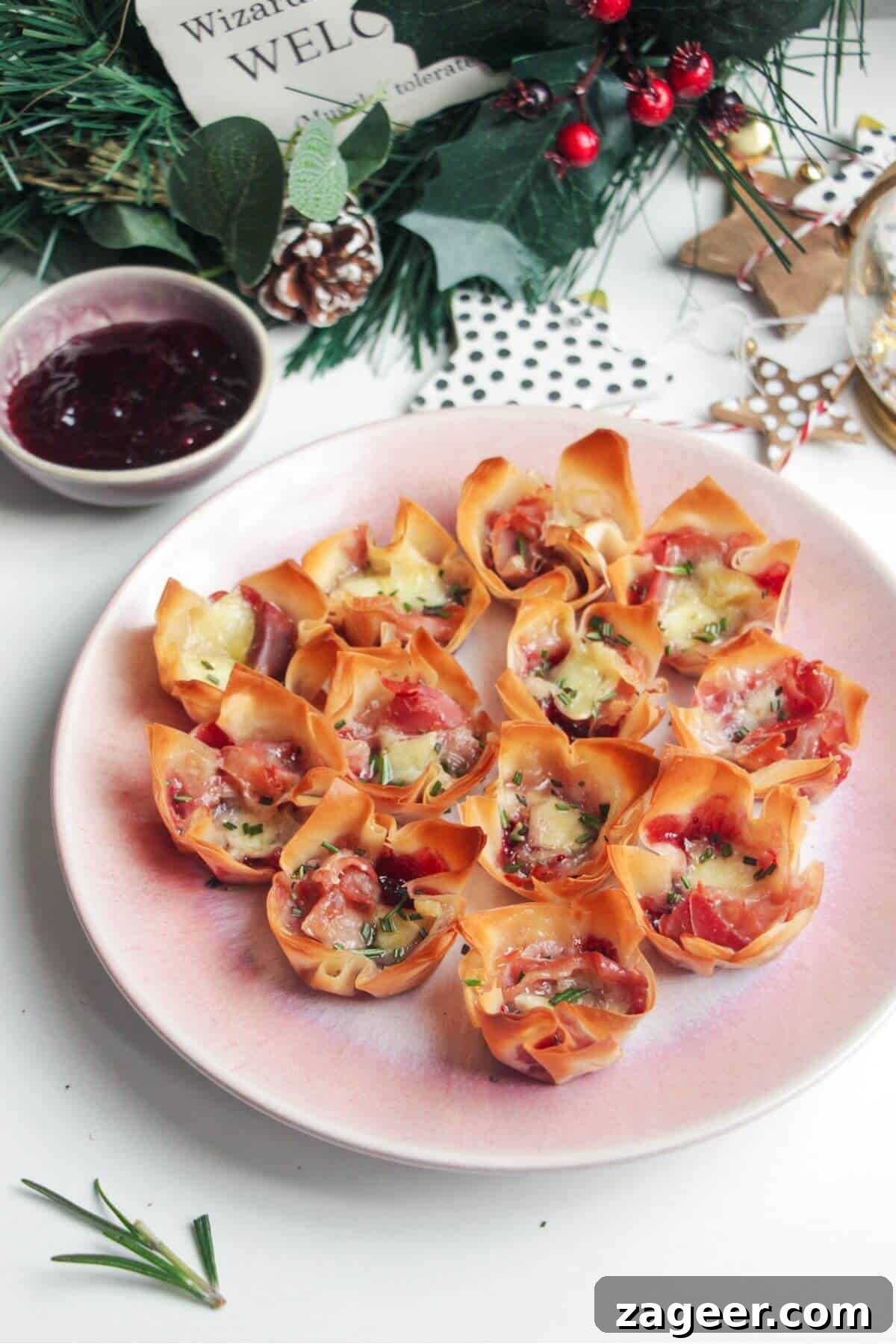 Effortless Brie, Cranberry, and Prosciutto Filo Parcels 2 Golden-brown Brie, Cranberry, and Prosciutto Filo Bites served on a small pink plate, showcasing their crispy edges and melted cheese, garnished with fresh rosemary.