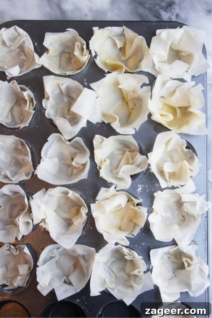 Effortless Brie, Cranberry, and Prosciutto Filo Parcels 5 Layered filo pastry squares carefully pressed into the cavities of a mini muffin tin to form small cups, showing the delicate folds.