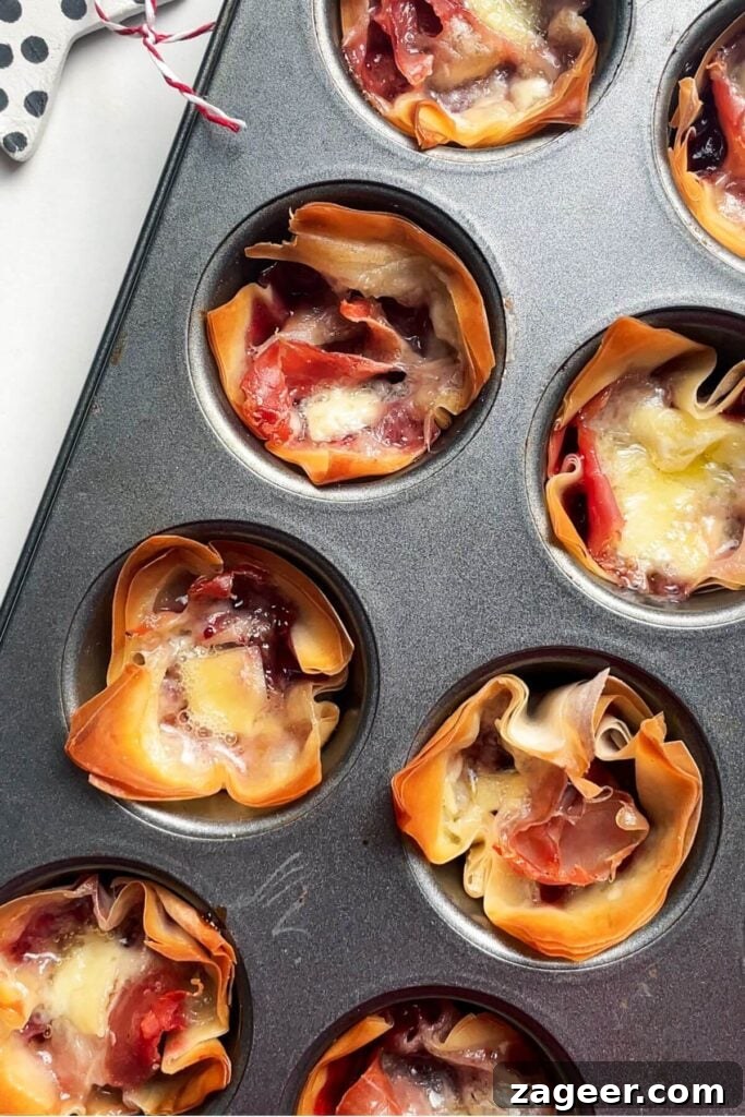 Effortless Brie, Cranberry, and Prosciutto Filo Parcels 7 Freshly baked Brie, Cranberry, and Prosciutto Filo Bites bubbling in a mini muffin tin, with golden-brown, crispy pastry and perfectly melted cheese, just out of the oven.