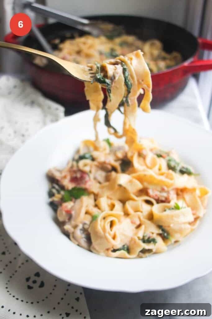 Creamy Miso Mushroom Fettuccine Alfredo 9 A fork lifting up a delectable swirl of mushroom Alfredo fettuccine from a deep bowl, garnished with fresh herbs and Parmesan.